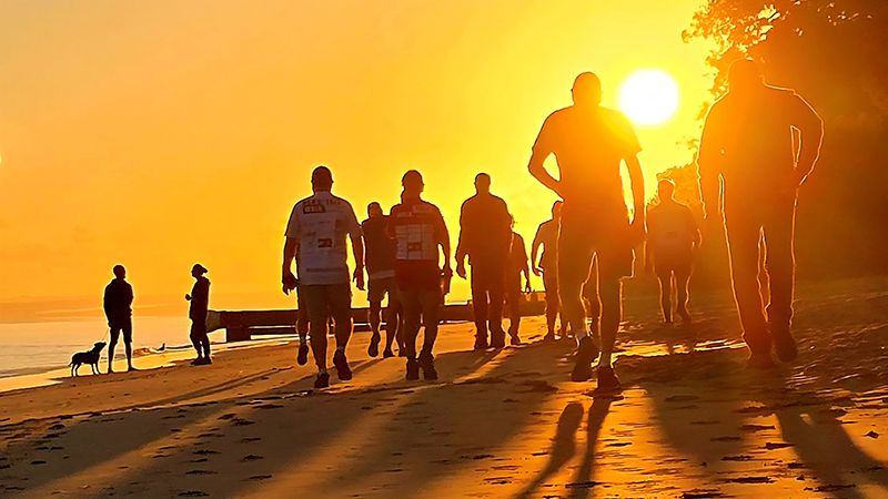 A walking group on the beach at sunrise